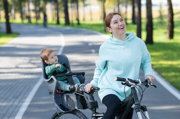 Obraz premium Caucasian woman riding a bicycle with her toddler son sitting behind her in a child seat. 