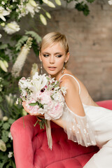 Beautiful bride with bouquet smiling in wedding dress sitting on bright pink sofa