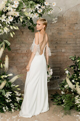 Beautiful young girl bride in her hands with a bouquet in a wedding dress at the arch