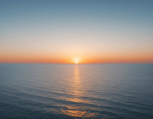 Fototapeta premium A serene sunset over the calm ocean, with a gradient of colors transitioning from warm orange and yellow to soft blue, reflecting beautifully on the water's surface.