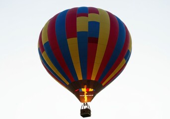 Naklejka premium A colorful hot air balloon with a flame against a bright white sky during the daytime hours seen up close