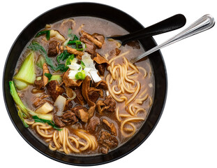 Deep clay bowl with noodle soup and boiled beef pieces. Traditional Chinese cuisine dish is decorated with greens and celery. Isolated over white background