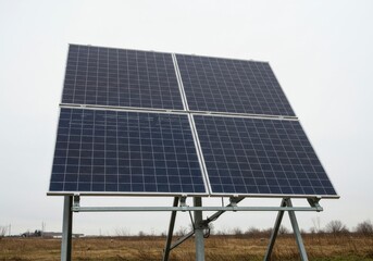 Four solar panels mounted on a metal frame stand in a field under an overcast sky on a cloudy day