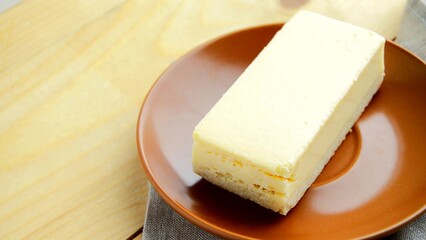 Laying out a brown plate with a rectangular slice of delicious cheesecake close-up on the table
