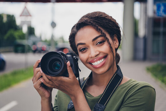 Charming young photographer with afro hairstyle smiling in urban setting holding camera outdoors on a sunny day