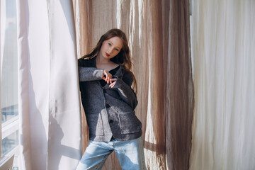 Obraz premium Beautiful blonde model, young girl, teenager in the studio in a jacket and jeans against the background of fluttering fabrics