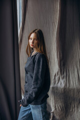Fototapeta premium Beautiful blonde model, young girl, teenager in the studio in a jacket and jeans against the background of fluttering fabrics