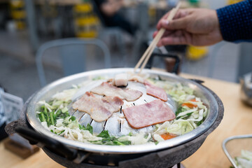 Unrecognizable man is enjoying cooking and eating Moo Ka Ta or Thai BBQ in outdoor restaurant