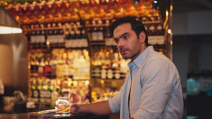Sitting smart man drinking alone of cocktail Old fashioned waiting friends or couple at bokeh lighting at luxurious beverage counter nightclub at pub and restaurant on Friday meeting night. Vinosity.