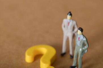 Businessmen Figurines Facing a Giant Yellow Question Mark – Concept of Decision-Making and Uncertainty