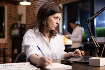 Closeup of caucasian woman working at her desk, focused on taking important notes on a notebook...