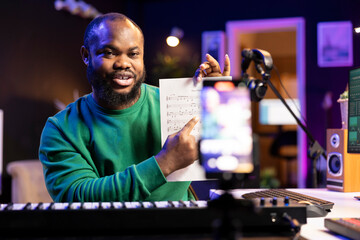 Singer producer showing musical sheet to explain notes on electronic keyboard, teaching how to play piano piano on a tutorial vlog in home studio. Performer musician presenting diatonic scale.