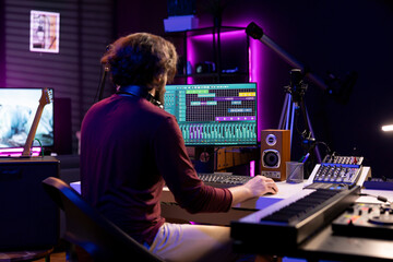 Sound engineer working in his home studio with daw software on computer and mixing tools, creating...