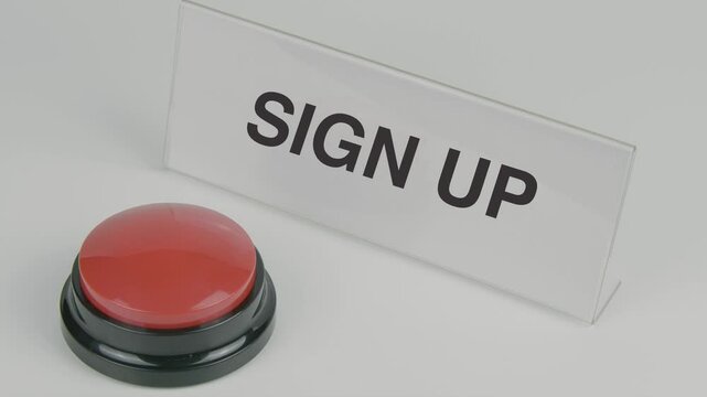 Sign up text or word displayed on a nameplate as a hand presses a red button set against a white background, encouraging registration for a service or offer