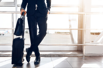 Business trip concept. Cropped of businessman standing by window in airport, holding luggage, copy...