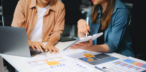 Fototapeta premium Two young business women sitting at table.colleagues working together, have a discussion and using tablet