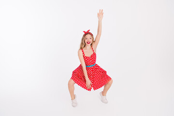 Cheerful young woman in retro polka dot dress enjoying playful dance with a raised hand on white...