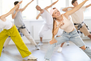 Naklejka premium Dynamic juvenile girl engaged in active dance together with other attendees of dancing courses