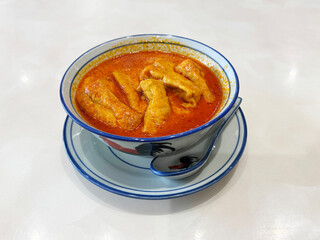 spicy nyonya noodle laksa curry soup with seafood prawn, fish cake, egg, bean curd and chilli sambal sauce in cock roster bowl on white marble table asian restaurant halal food cafe menu