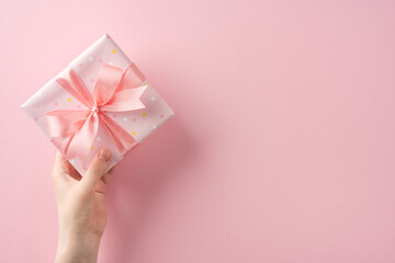 Hand presenting a beautifully wrapped pink gift with ribbon against a matching pink background