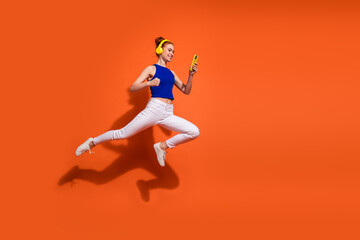 Young woman jumping joyfully while listening to music on headphones and using a smartphone