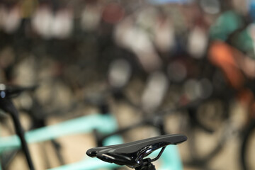 Close-up view focusing on black bike saddle with blurred backdrop of numerous bicycles in cycling store