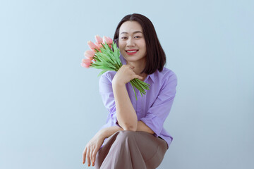 Young woman with flowers smiles cheerfully in a light blue setting during springtime