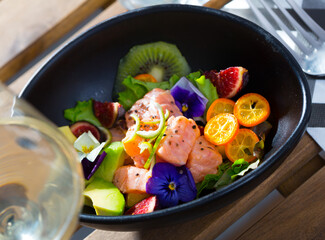 Exotic ceviche of salmon served with fresh avocado, cumquat, kiwi fruit, figs decorated with pansy flowers