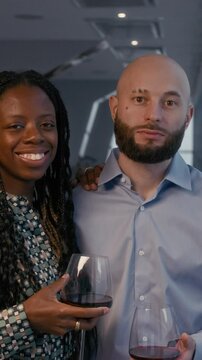 Vertical portrait of elegant diverse couple looking at camera with red wine in restaurant