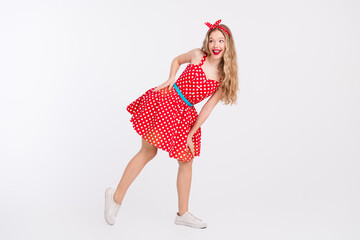 Joyful young woman in retro polka dot dress posing playfully on white background full of energy and...