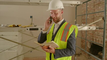 A dedicated professional in a hard hat and safety vest is on a work call, reviewing notes at a busy construction site to ensure smooth operations and maintain safety and productivity