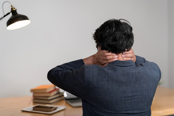 Obraz premium Neck ache concept. Young man sitting at office desk feeling hurt having pain in his neck.
