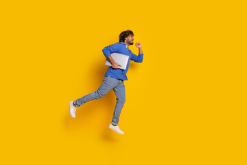 Young stylish man in trendy casual outfit running against vibrant yellow background holding laptop, representing active lifestyle