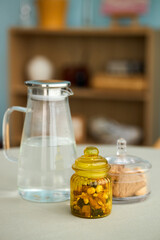 Close-up view of a jar of homemade candied fruits, a carafe of water and plate of cookies set on...