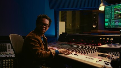 Music producer operating mixing console in control room and working with audio recording software...