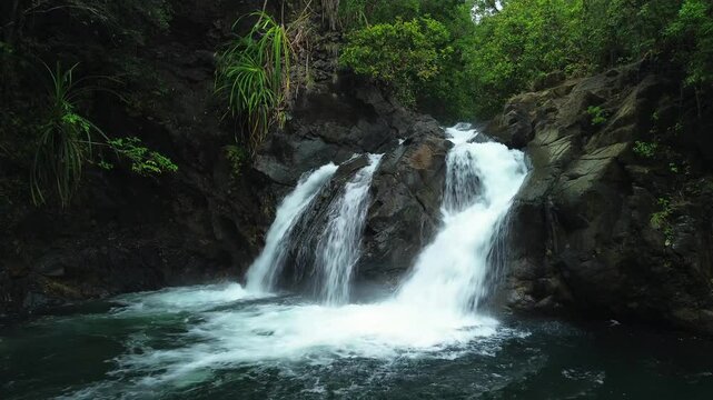 Close view of Estrella Waterfall in Narra Palawan with white water rushing over dark rocks into a forest pool surrounded by tropical greenery