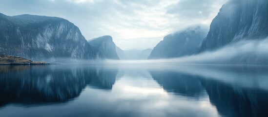 Fototapeta premium Misty fjord mountains reflecting in calm water. Peaceful nature scene