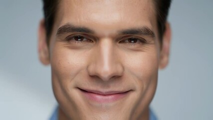 Closeup portrait of young man's face with brown eyes looking directly at camera with slight smile against grey background, conveying confidence, attractiveness and positive expression concept