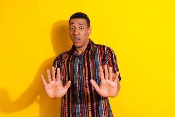Young man expressing awe with gesture while wearing stylish print shirt against bright yellow...