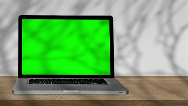 a laptop with green screen outdoors, trees swaying in the background.