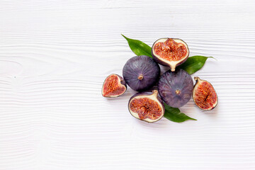 Fresh ripe figs whole and cut with green leaves on wooden table. Top view