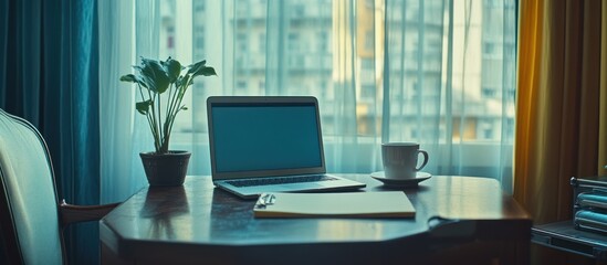 Fototapeta premium Laptop, coffee, plant on desk, city view. Work from home