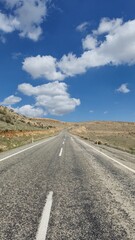 an asphalt road marked with white lines against cloudy blue sky