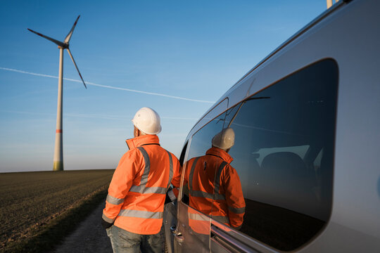 Engineer inspecting wind turbine with reflection in car window