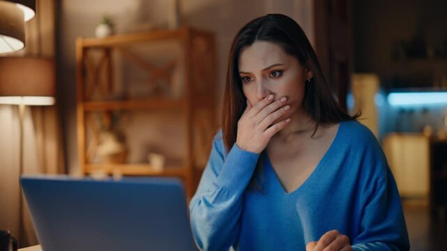 Concerned brunette reading email at laptop in dark home closeup. Desperate woman