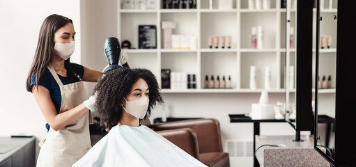 After pandemic reality. Young woman and hairdresser wearing protective masks during beauty...