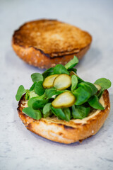 Des feuilles de salade fraîches et des cornichons tranchés sont disposés sur le pain burger pour apporter croquant et fraîcheur.