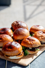 Vue sur plusieurs hamburgers faits maison avec des steaks, de la salade, du fromage fondant, le tout disposé sur une planche en bois.