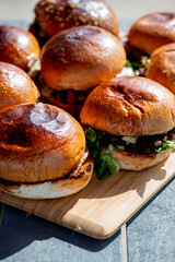 Vue sur plusieurs hamburgers faits maison avec des steaks, de la salade, du fromage fondant, le tout disposé sur une planche en bois.