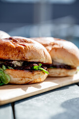 Vue sur plusieurs hamburgers faits maison avec des steaks, de la salade, du fromage fondant, le tout disposé sur une planche en bois.